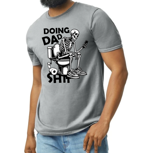 Image of a T-shirt depicting a humorous graphic of a skeleton sitting on a toilet while using a phone. The text ‘Doing Dad Sh*t’ is prominently displayed above the graphic. The T-shirt is shown in four color options: vibrant red, classic gray, bold blue, and fresh green, highlighting its availability for different preferences. A perfect blend of comfort and dad-style humor, suitable for various casual occasions.